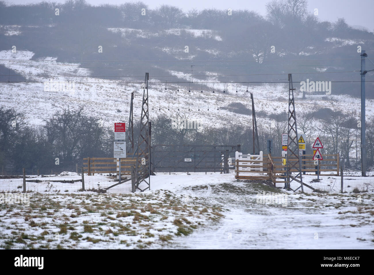 Unbeaufsichtigte Bahnübergang im Winter mit Schnee auf dem Boden. Unkontrollierte Tore in einem Feld. C2C-Linie durch Hadleigh Country Park. Hügel Stockfoto