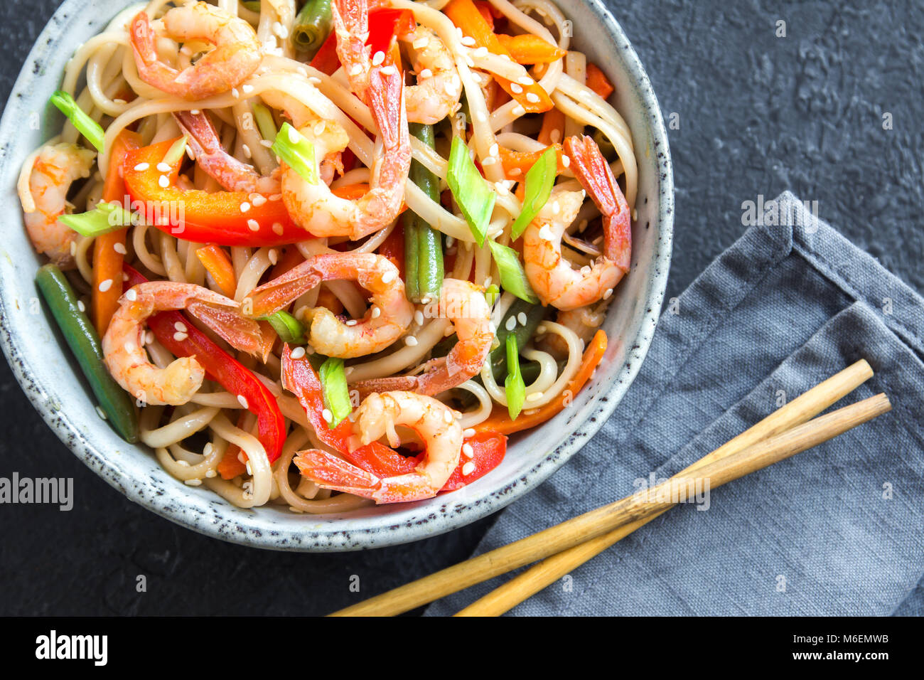 Pfannengerichte mit Udon-nudeln, Shrimps (Garnelen) und Gemüse. Asiatische gesundes Essen, Mahlzeit, Braten in der Schüssel verrühren über schwarzen Hintergrund, kopieren. Stockfoto