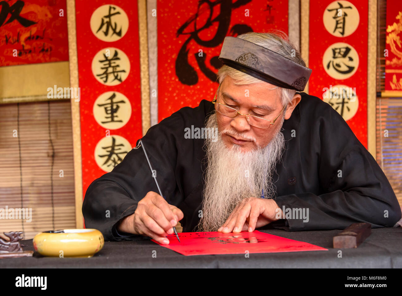 Eine ältere vietnamesischen Mann mit einem langen weißen Bart verwendet eine Bürste chinesische Zeichen zu zeichnen Kalligraphie in Hanoi, Vietnam Stockfoto