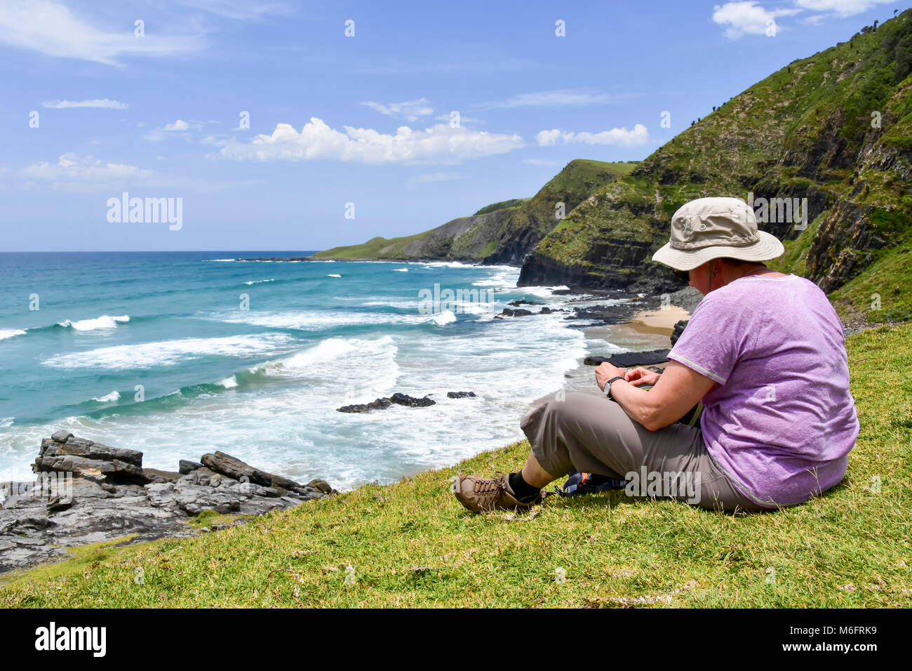 Eine weibliche Wanderer sitzen mit Blick auf die Küstenlinie auf den Spuren von Coffee Bay am Indischen Ozean im östlichen Kap an der wilden Küste von South Af Stockfoto