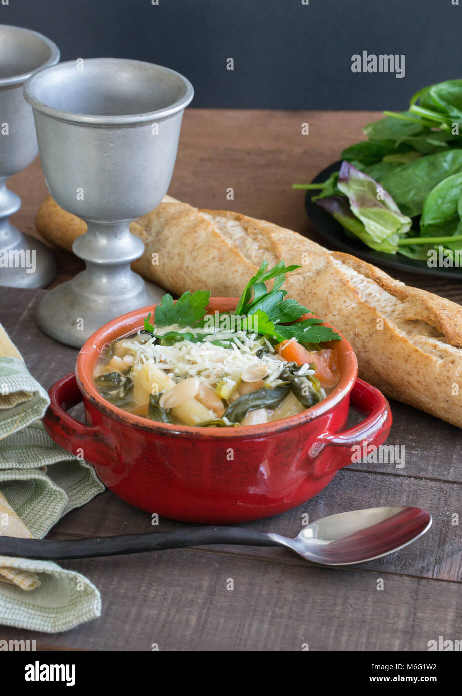 Herzhaftes aus weißen Bohnen und Gemüse Suppe Eintopf serviert in einem roten Topf mit einem Laib Weizen französischem Brot. Essen Szene, hausgemachte Güte. Stockfoto