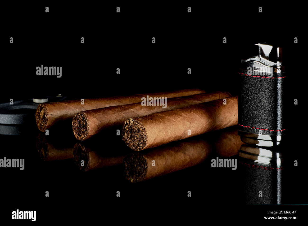 Zigarre mit Cutter und leichter, auf einem Glastisch auf schwarzem Hintergrund reflektiert Stockfoto