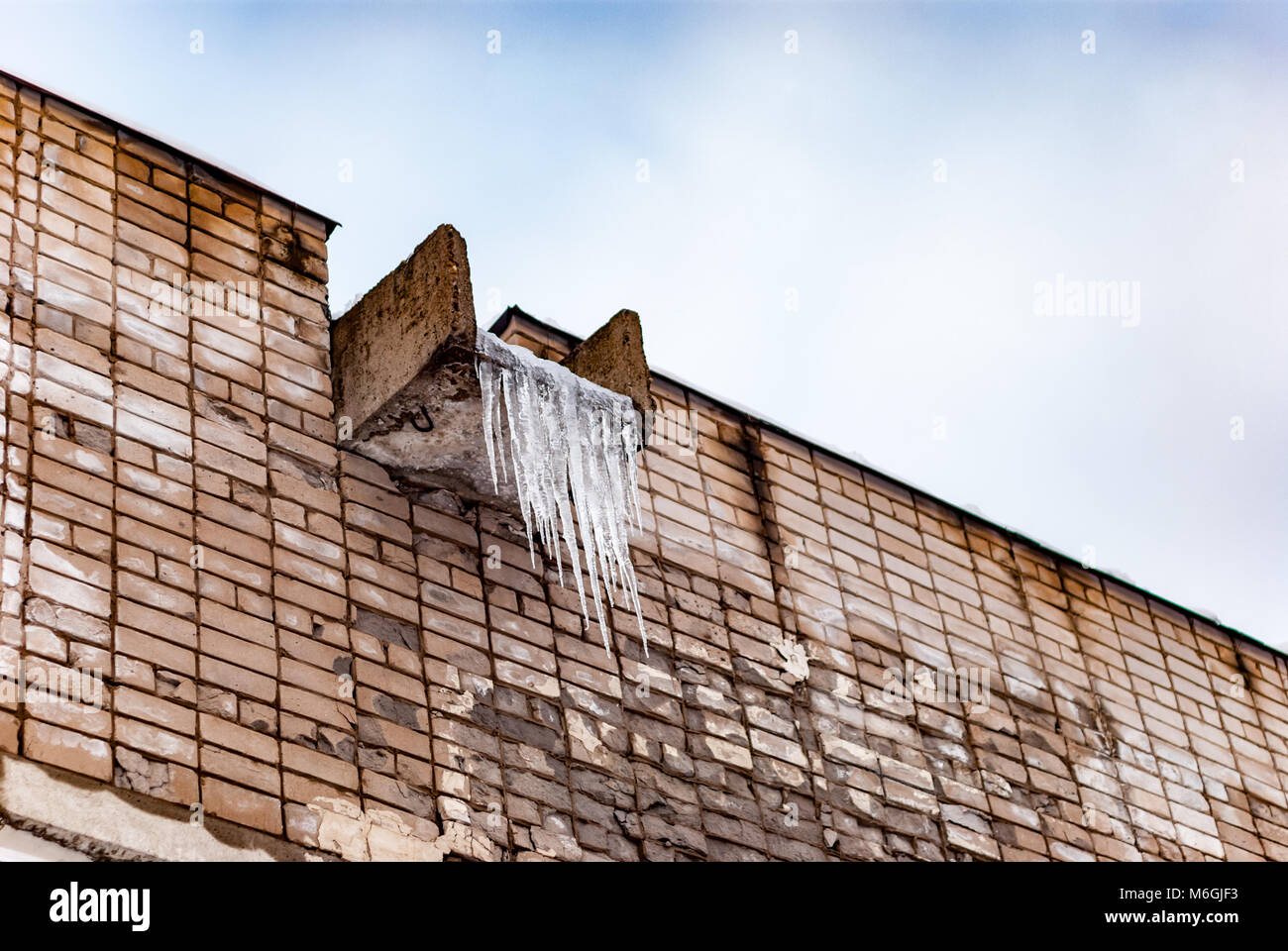 Gefrorene Eiszapfen hängen an einem Betontrog auf einer alten Ziegelmauer, Überreste der Winterkälte Stockfoto