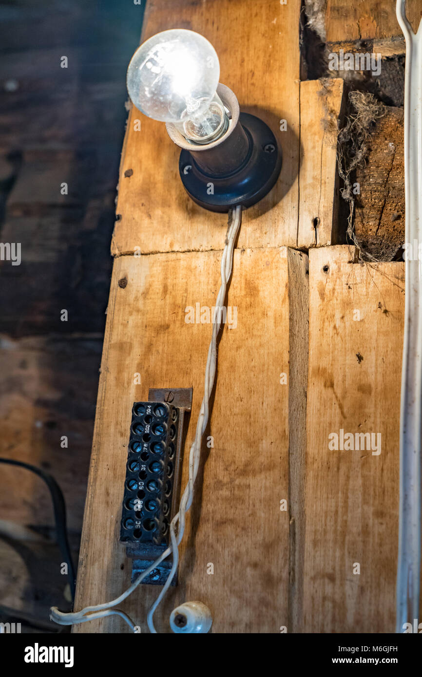 Antike elektrische Klemme gepaart mit einer glühenden Glühlampe erinnert an den Charme einer vergangenen Ära in der Fachwerkkulisse eines malerischen Holzhauses Stockfoto