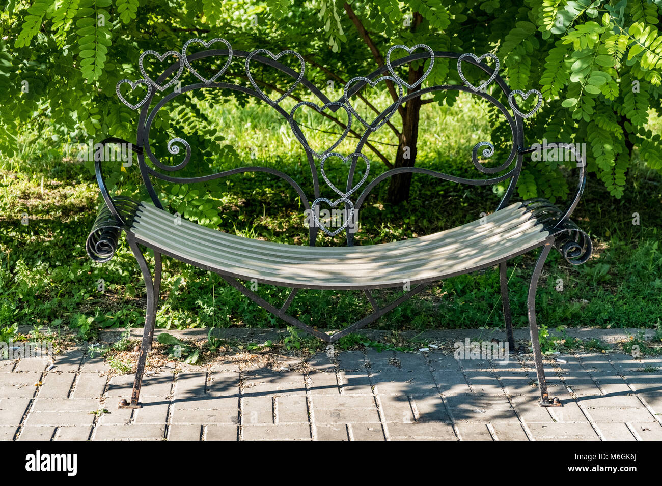 Eine aufwändig gefertigte schmiedeeiserne Lovers Bank, perfekt für eine romantische Pause in der ruhigen Atmosphäre eines Parks Stockfoto