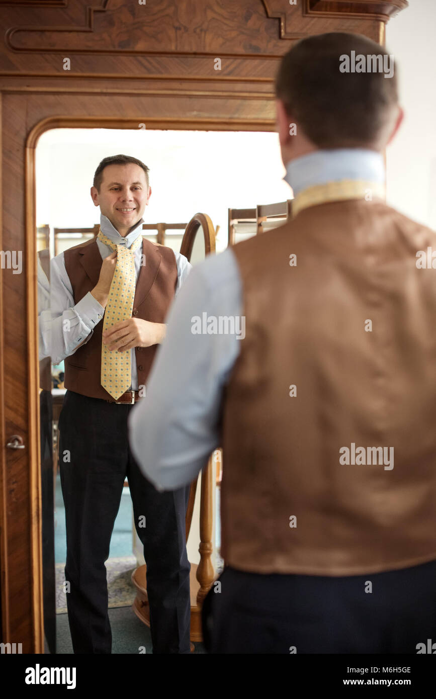 Elegante Mann mit Weste tieing Krawatte beim Stehen vor der Spiegel Stockfoto