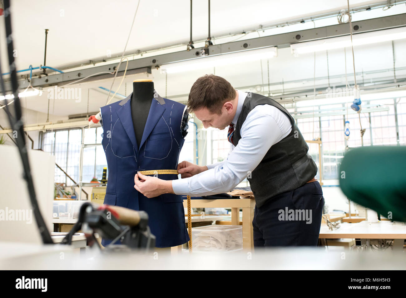 Maßgeschneiderte messen eine unvollständige Jacke auf eine Schaufensterpuppe mit einem Maßband, wie er in seiner Werkstatt arbeitet Stockfoto