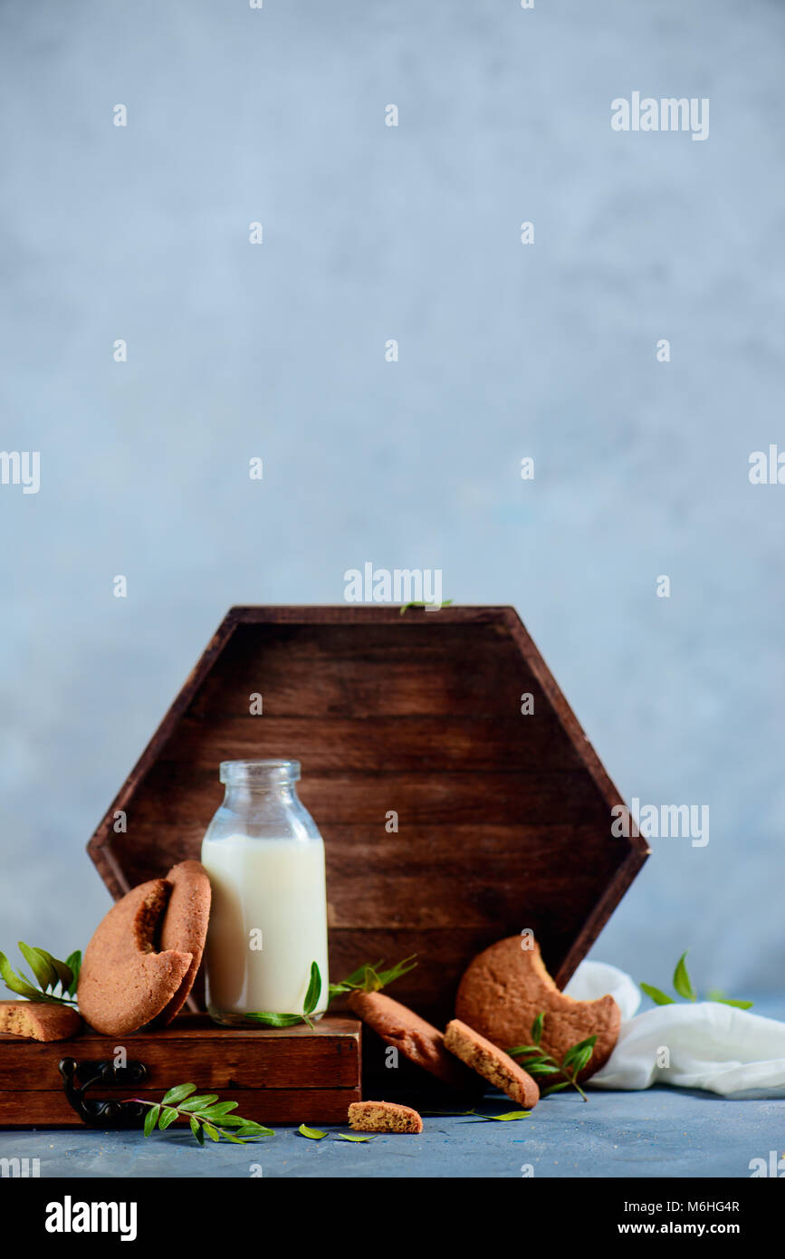 Gesundes Frühstück Konzept mit Haferflocken Kekse, eine Flasche Milch, eine hölzerne Fach und Pistazien Blätter auf einen hellen grauen Stein Hintergrund. Leckere hausgemachte Stockfoto