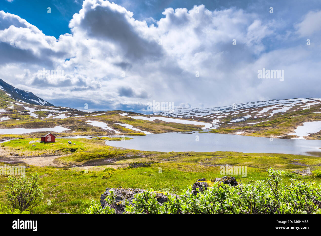 Rote Hütte an einem Bergsee, Norwegen, umgeben von schneebedeckten Bergen im Sommer, Nord-Norwegen, Vikafjell Stockfoto