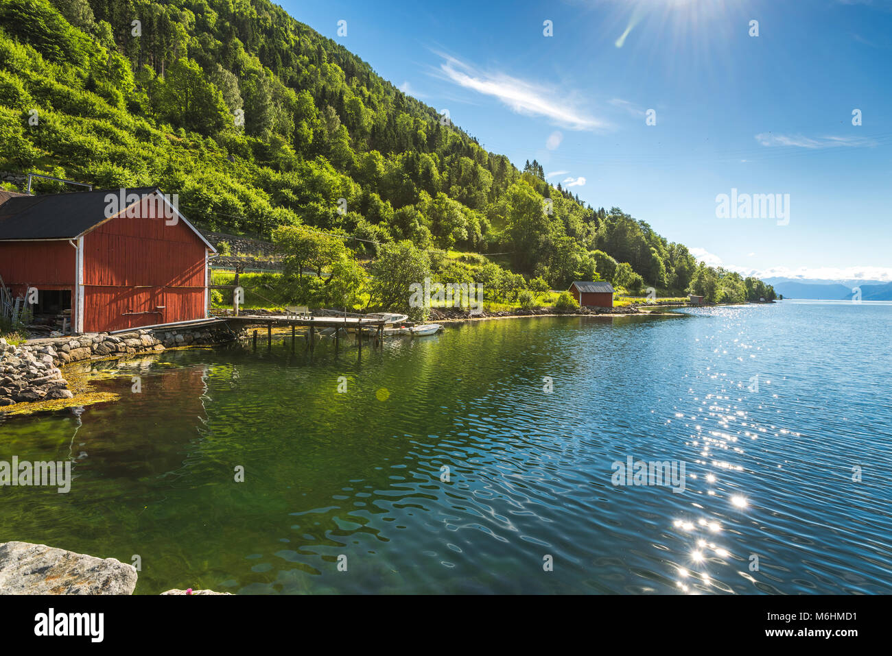 Ufer des Fjords mit Bootshäuser, Eidfjord, Norwegen, Fjord Landschaft am Esefjorden mit Sun Reflexionen auf dem Meer Stockfoto