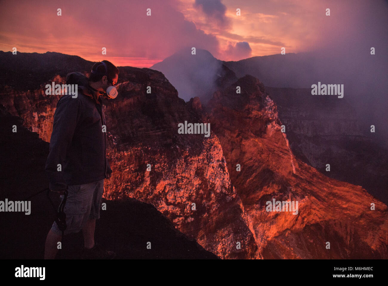 Ein Besucher, beleuchtet vom Licht der Vulkan, lehnt sich über und blickt in die Krater des Marum, die hält einen Lavasee, 400 Meter nach unten, einer von nur einer Hand Stockfoto