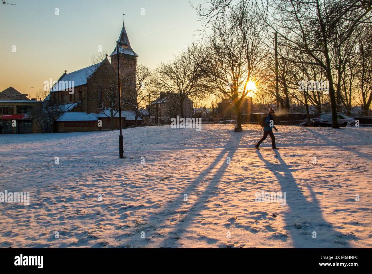 Eine Person Wanderungen durch den Schnee Kirchhof bei Sonnenaufgang abgedeckt Stockfoto