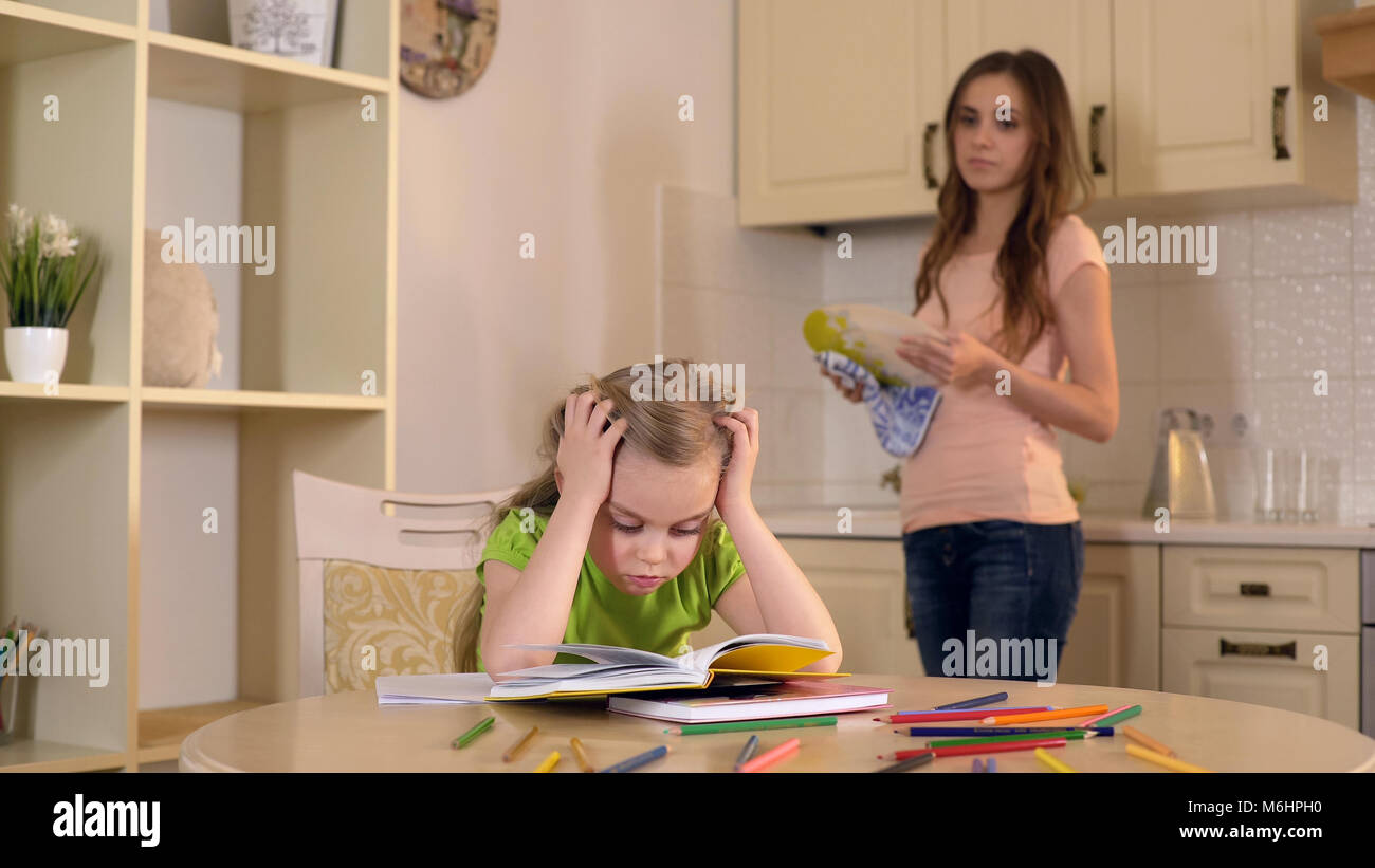 Mom Geschirr aufpassen als Tochter ihre Hausaufgaben mit Schwierigkeiten Stockfoto