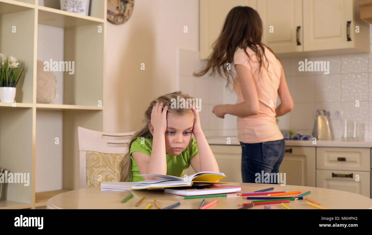 Frau ist in der häuslichen Pflichten eingeschaltet, während ihre Tochter tun langweilig Hausaufgaben Stockfoto