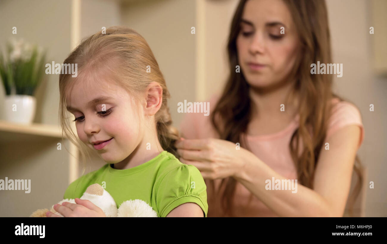 Fürsorgliche Mutter flechten glücklichen kleinen Töchter Haar, die Betreuung ihres Kindes Stockfoto