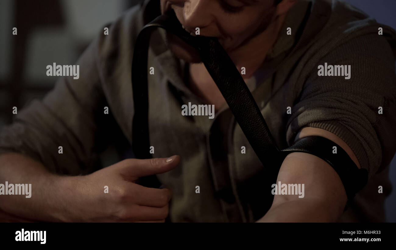 Männliche junkie Holding tourniquet mit seinen Zähnen, die Vorbereitung auf die Droge Einspritzanlage Stockfoto