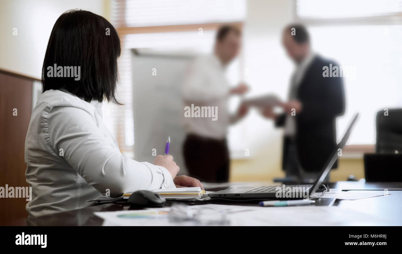 Frau sitzt am Tisch in der Sitzung, an der Kollegen argumentieren über Projekt suchen Stockfoto