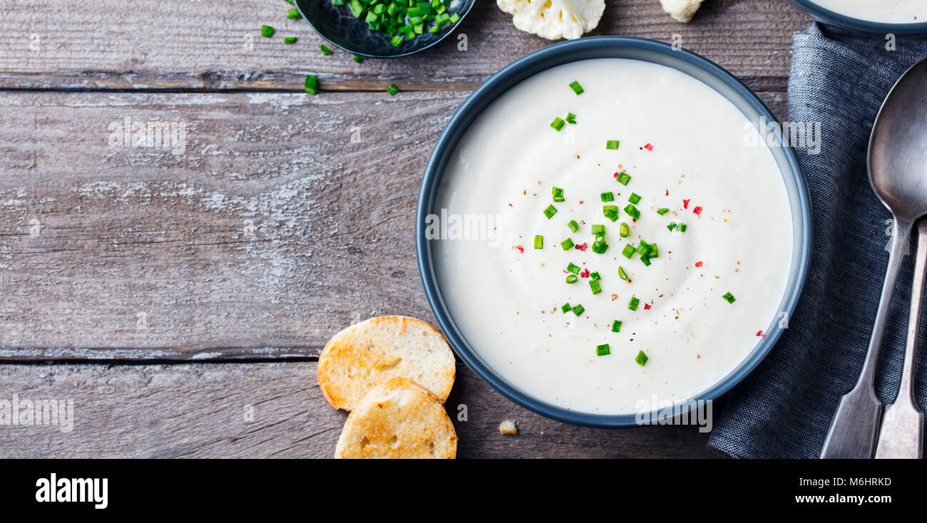 Blumenkohl, Kartoffel Cremesuppe mit Frühlingszwiebeln in Schale schwarz auf grau Holz- Hintergrund. Kopieren Sie Platz. Stockfoto