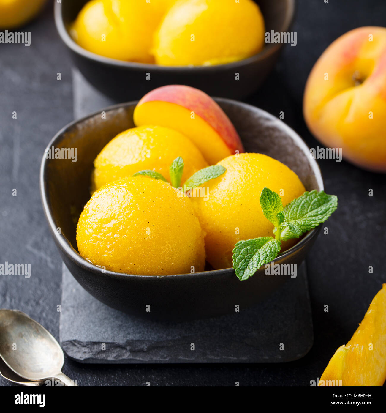 Mango, Pfirsich Eis, Tropical Fruit Sorbet in schwarz Schüssel auf Stein. Stockfoto