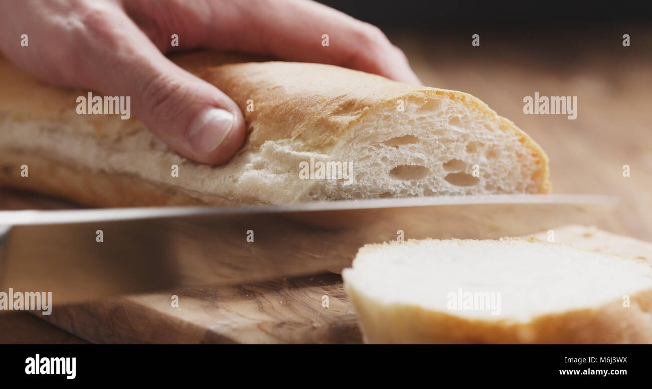 Closeup Mann slicing Baguette auf Holzbrett Stockfoto