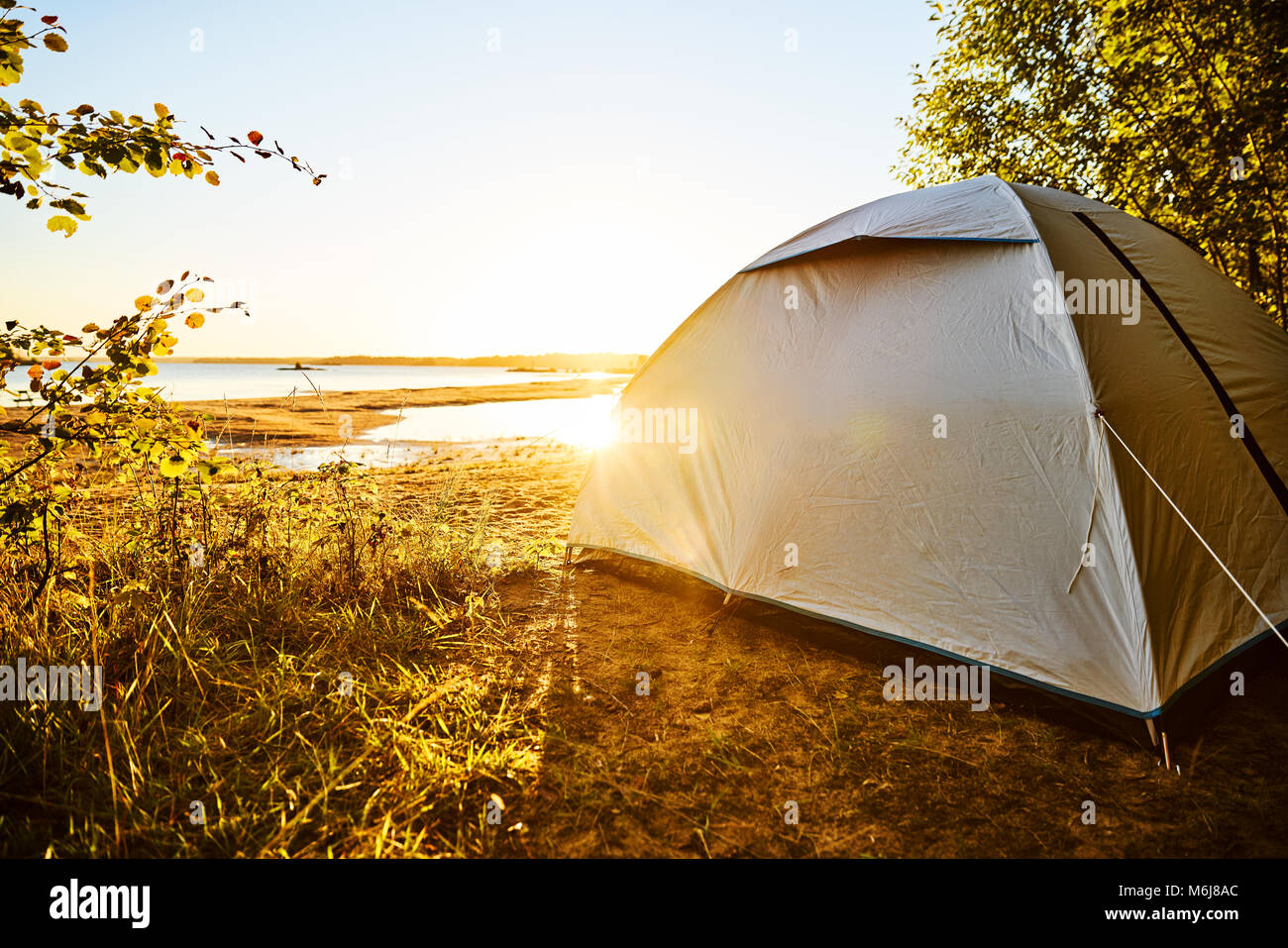 Weiße Zelt an einem Strand Campingplatz am See Vänern in Schweden. Die Sonne scheint und bald wird Sonnenuntergang. Sun Spiegelungen im Wasser. Stockfoto