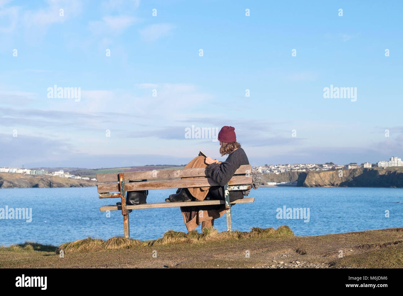 Eine Frau, die alleine auf einer Bank sitzen, ein Buch lesen zu wenig Fistral in Newquay Cornwall. Stockfoto