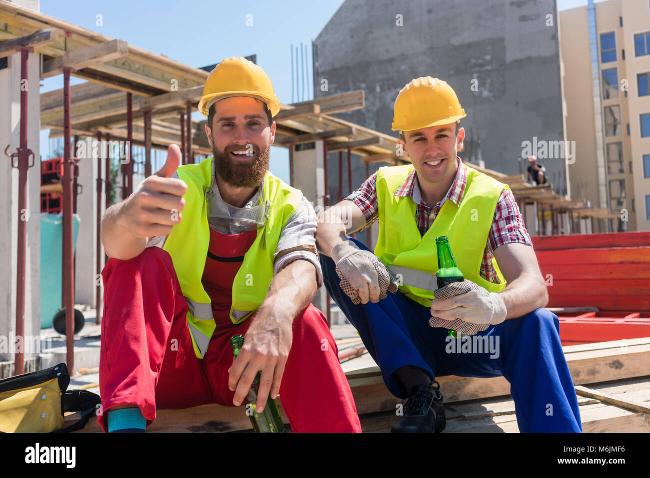 Zwei junge Arbeiter trinken ein kaltes Bier in der Pause bei der Arbeit Stockfoto