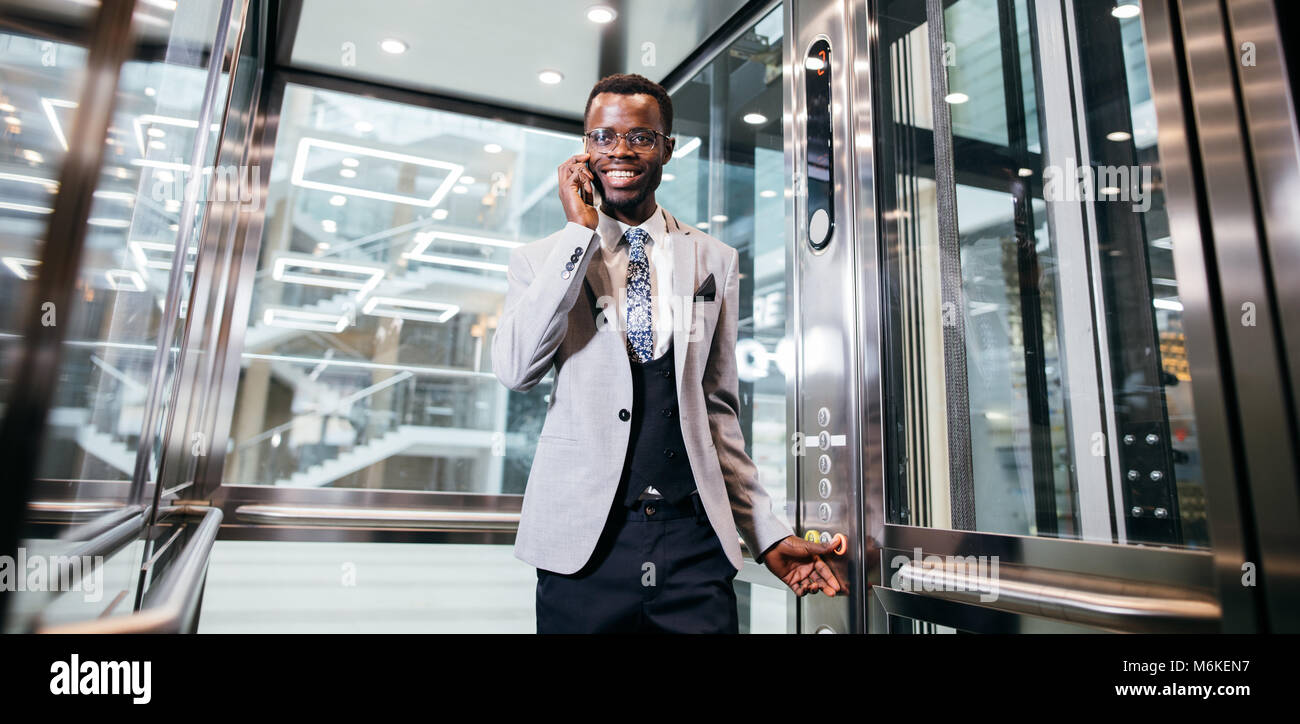 Afroamerican Geschäftsmann in der modernen Aufzug aus Glas am Telefon sprechen Stockfoto