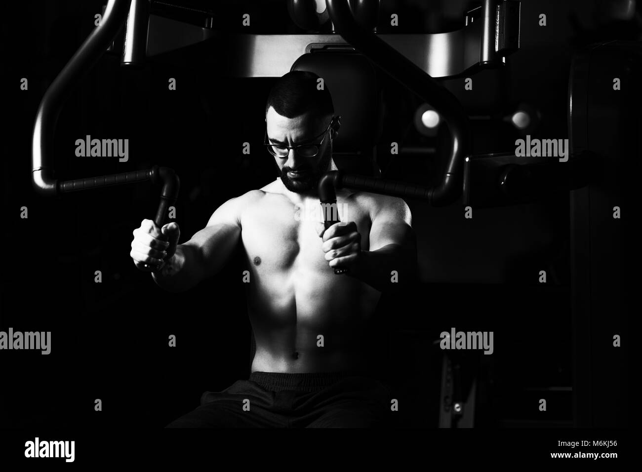 Schöne muskulöse Fitness Mann mit Brille, Schwere Übung für Brust, auf dem Rechner mit Kabel in der Turnhalle Stockfoto