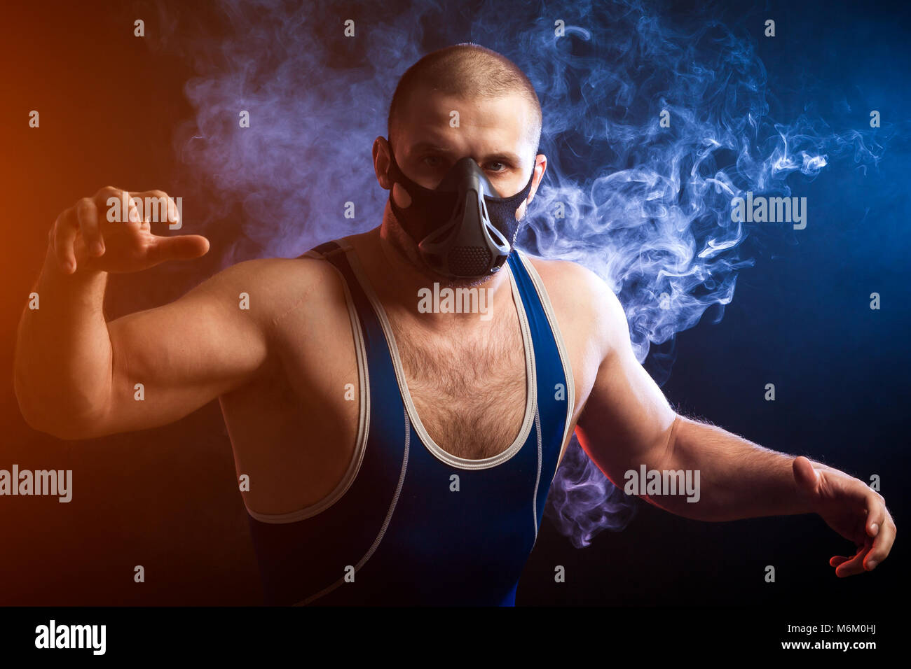 vapen und sport Ein junger sportlicher Mann Wrestler in einem grünen Sport Shirt und  trainieren Maske wrestling vor einem blauen Hintergrund vape Rauch auf  einem schwarzen isoliert Stockfotografie