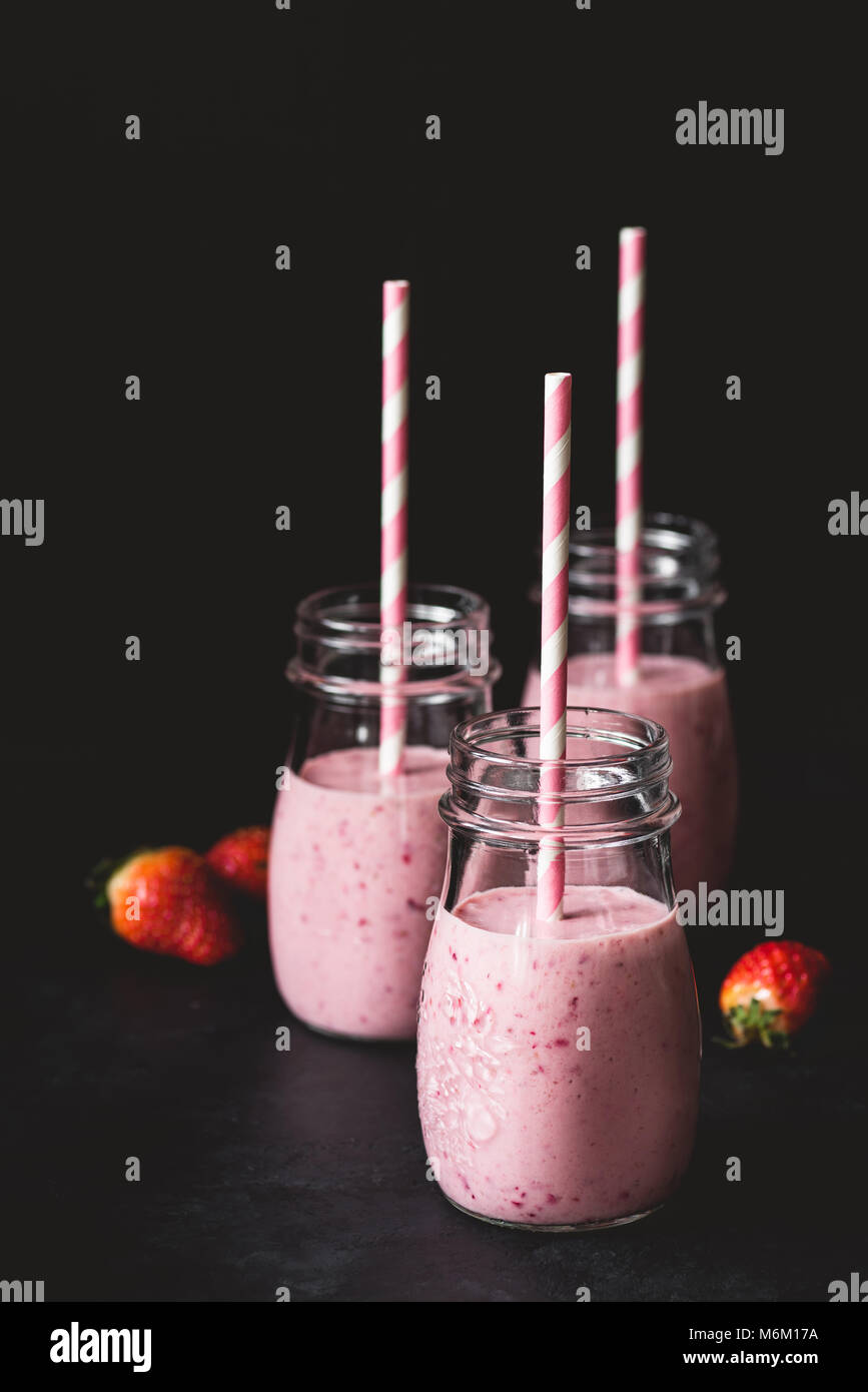 Frische Erdbeeren Smoothies in Gläsern mit rosa Strohhalm auf dunklem Hintergrund, selektiver Fokus und kopieren Sie Platz für Text. Gesunder Lebensstil, Fitness, d Stockfoto