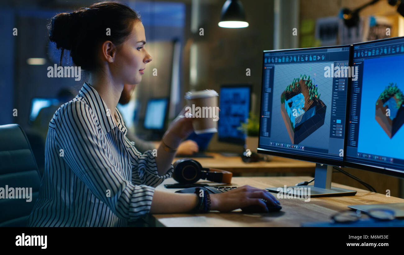 Weibliche Spiel Entwickler arbeitet auf einem Level Design auf Ihrem eigenen Computer mit zwei Displays, arbeitet sie spät und trinkt Kaffee. Kreative Loft Büro Stockfoto
