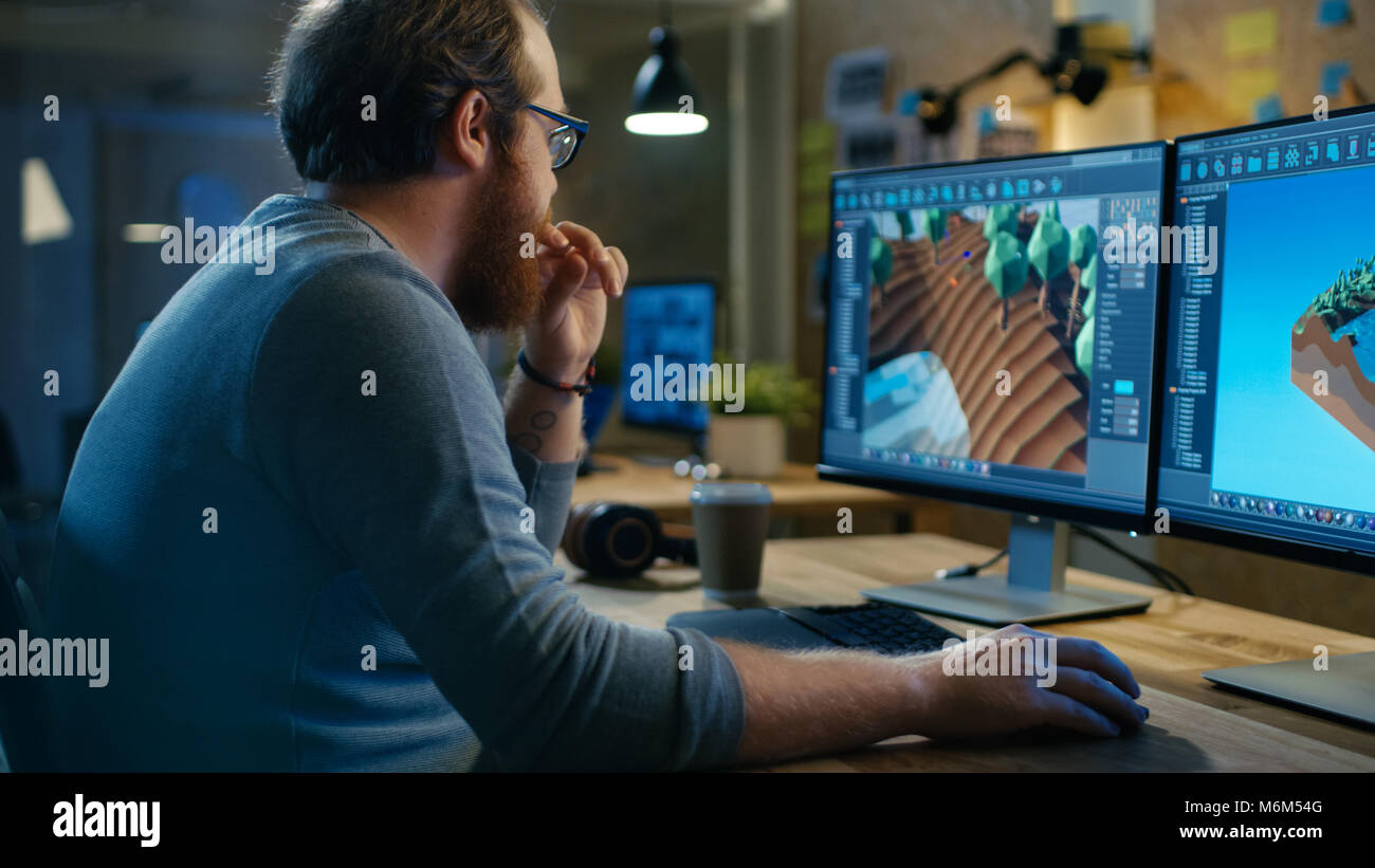 Kreative männlichen Spiel Entwickler arbeitet mit Grafiken für das neue Design, sitzt er an seinem Tisch an zwei Anzeigen Personal Computer. Stockfoto