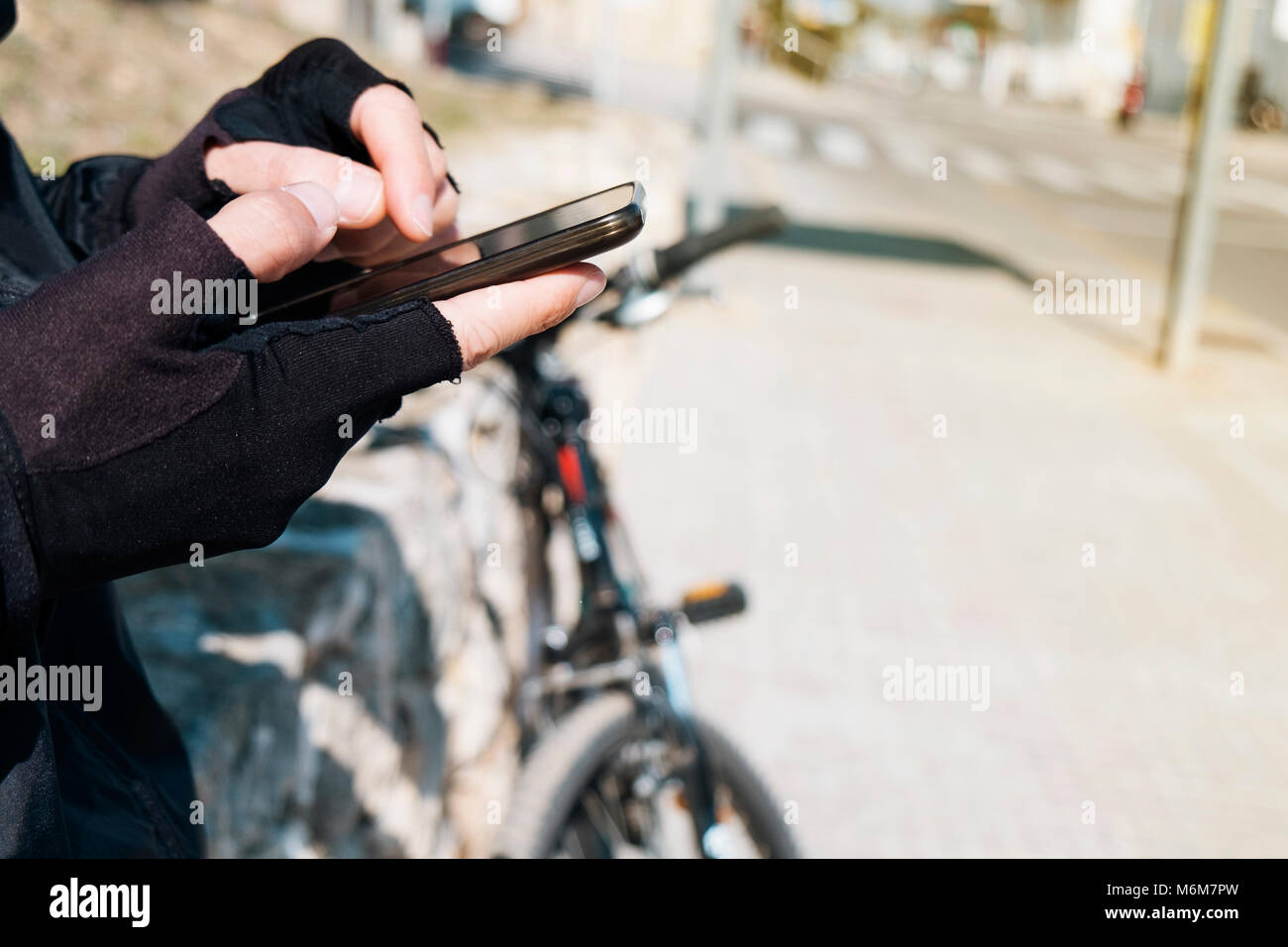 Nahaufnahme eines jungen kaukasischen Radfahrer Mann mit Fahrrad Handschuhe mit seinem Smartphone Neben seinem Fahrrad im Freien Stockfoto
