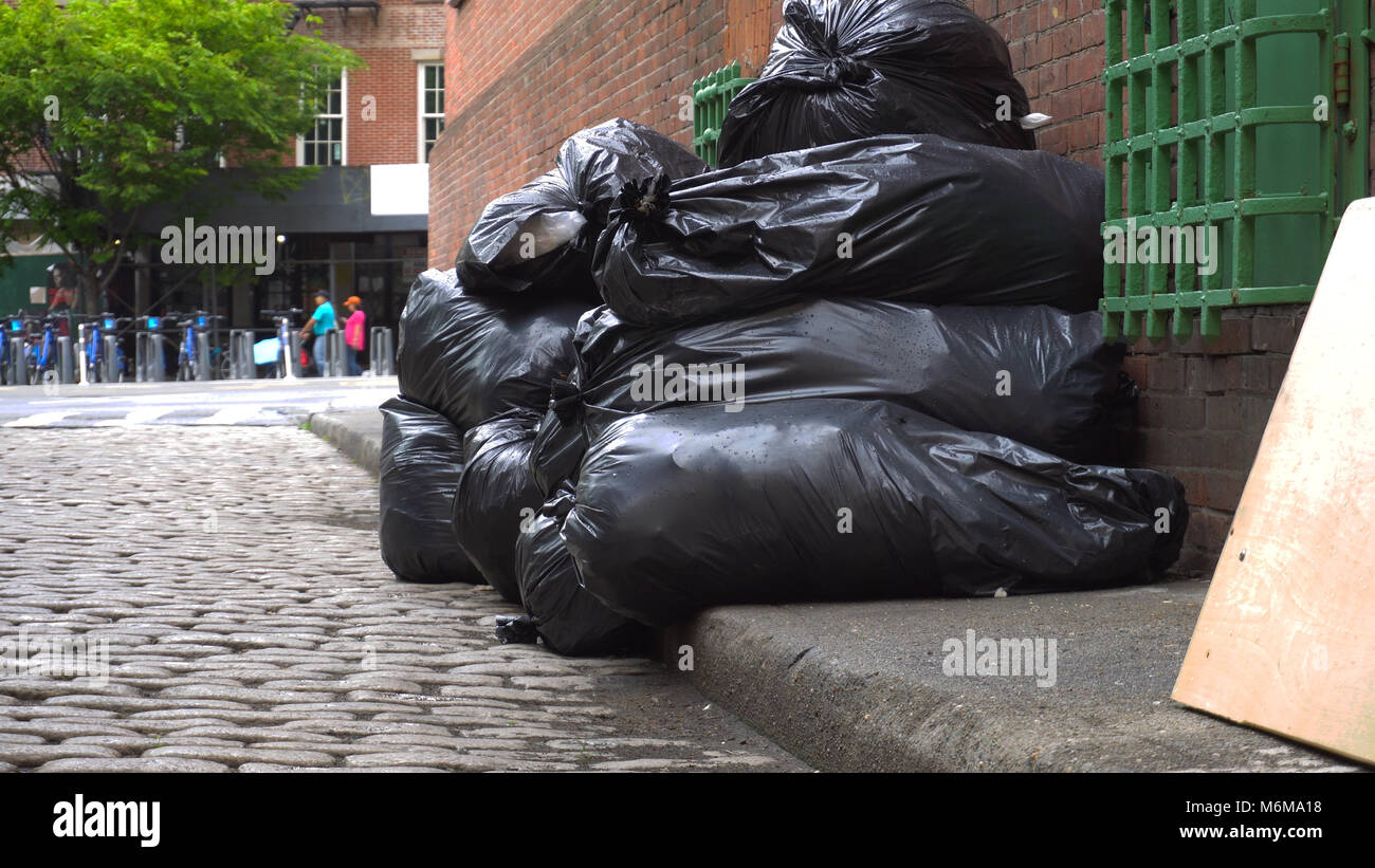 Schwarze Müllsäcke sitzen entlang einer ruhigen Strasse der Stadt warten, von sanitären Einrichtungen gesammelt werden. Niedrigen Winkel zur Gründung Bild mit einem Brooklyn Straße in Th Stockfoto