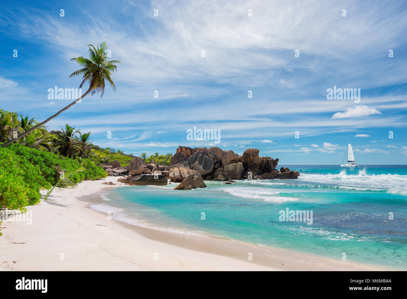 Tropischer Strand mit Palmen und ein Segelboot im Meer, La Digue, Seychellen. Stockfoto Tropischer Strand mit Palmen und ein Segelboot im Meer, La Digue, Seychellen. Stockfoto