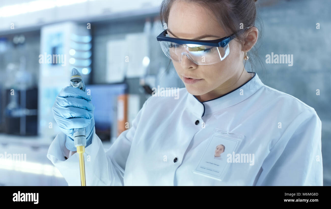 Weibliche Wissenschaftler verwendet Mikropipette Füllung Röhrchen in einem großen modernen Labor. Im Hintergrund arbeiten die Wissenschaftler im Computer. Stockfoto