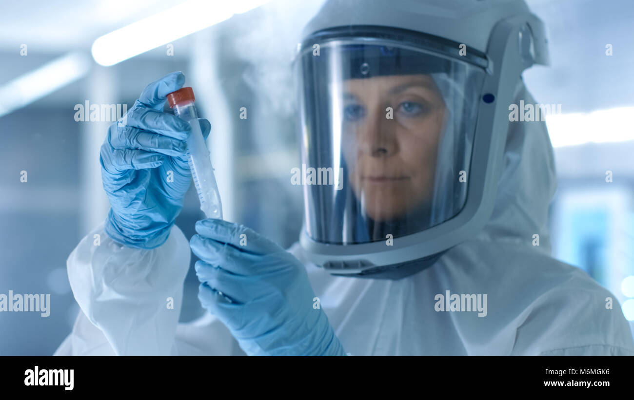 Medizinische Virologie Wissenschaftler arbeitet in einem Gefahrgut-Anzug mit Maske, inspiziert Reagenzglas mit isolierten Virus String aus dem Kühlschrank. Stockfoto