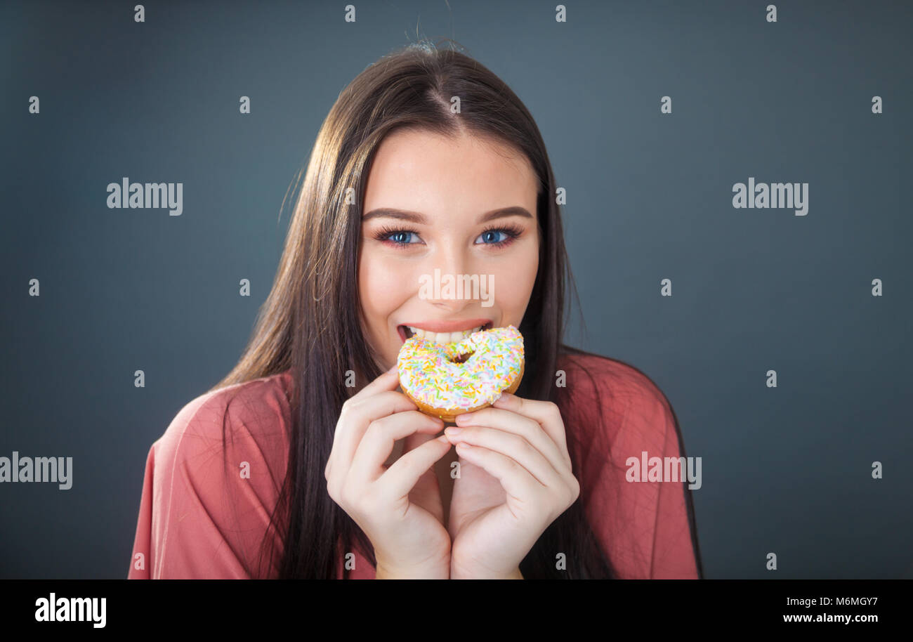 Hübsches junges Mädchen halten und nimmt einen Bissen von einem Donut. Stockfoto