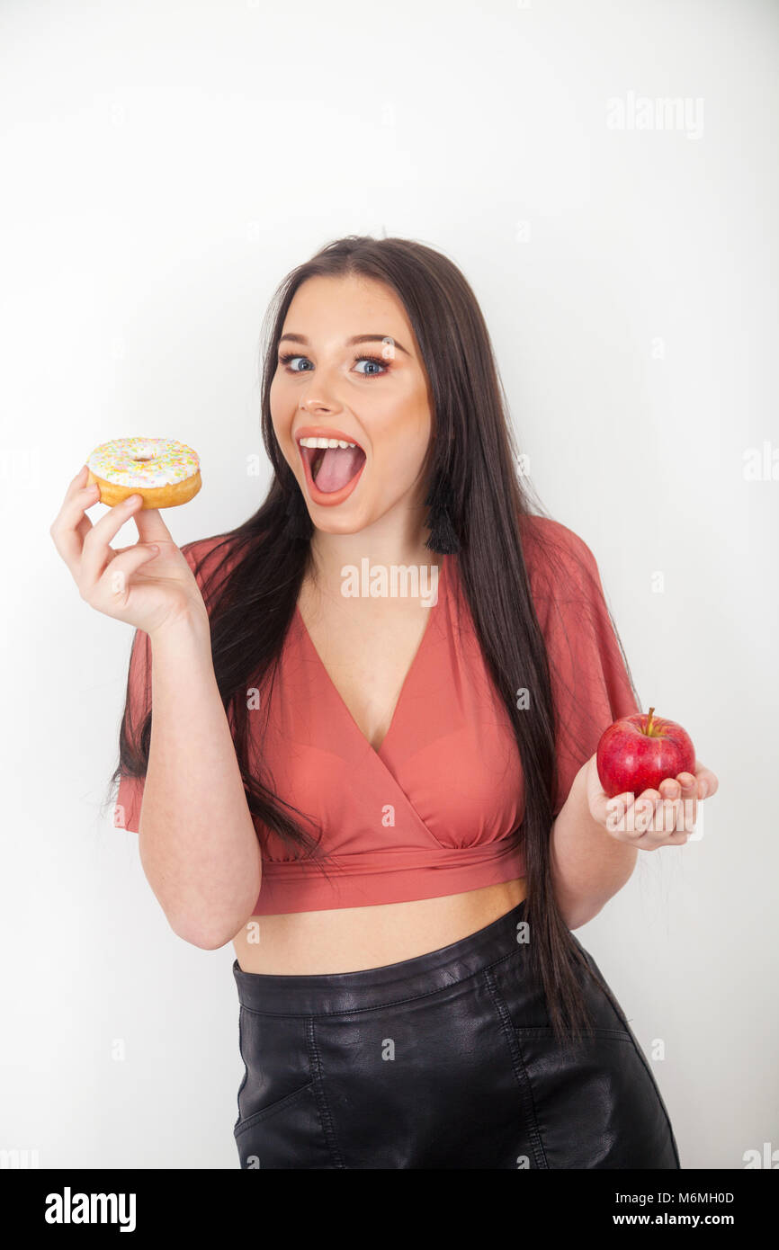 Hübsches junges Mädchen mit einem Apfel in der einen Hand und ein Donut in der anderen. Stockfoto