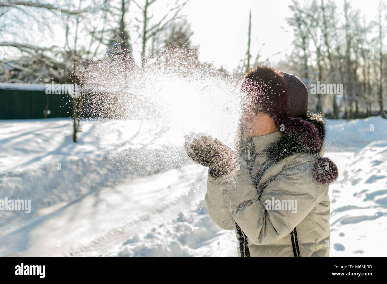 Hält eine Frau eine Handvoll Schnee in den Händen und bläst. Winter im Wald. Die sonne funkelt. Tag, Russland. Stockfoto