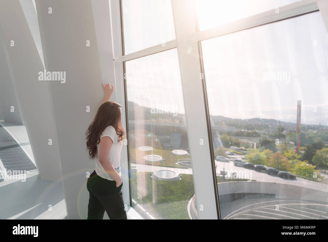 Junge, attraktive Frau, in einem modernen Gebäude, leger gekleidet, freuen uns auf ein großes Fenster mit der Sonne über ihre leuchtenden. Stockfoto