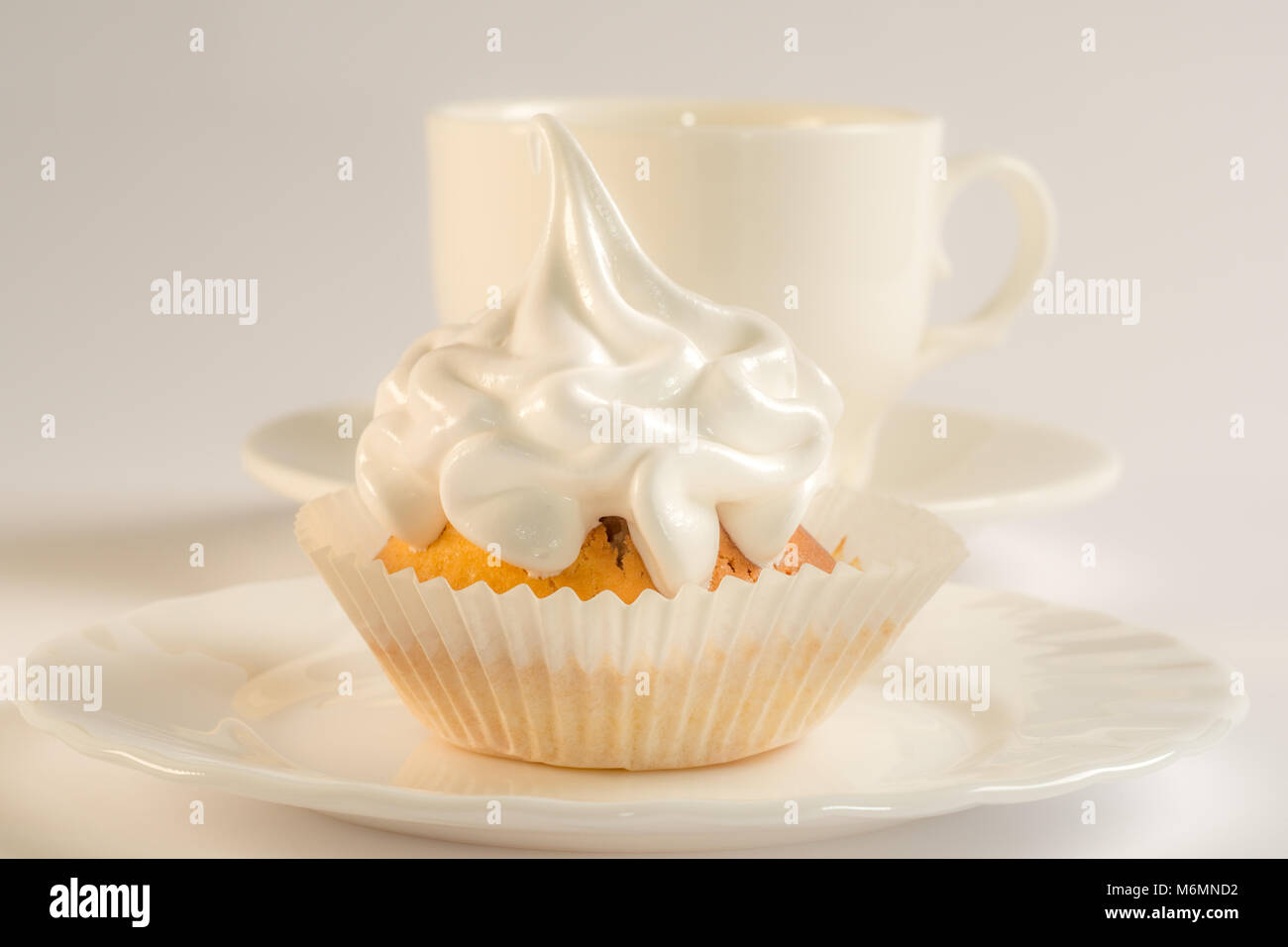 Cupcake mit weißer Zuckerglasur auf einen Teller und eine Tasse Kaffee ...