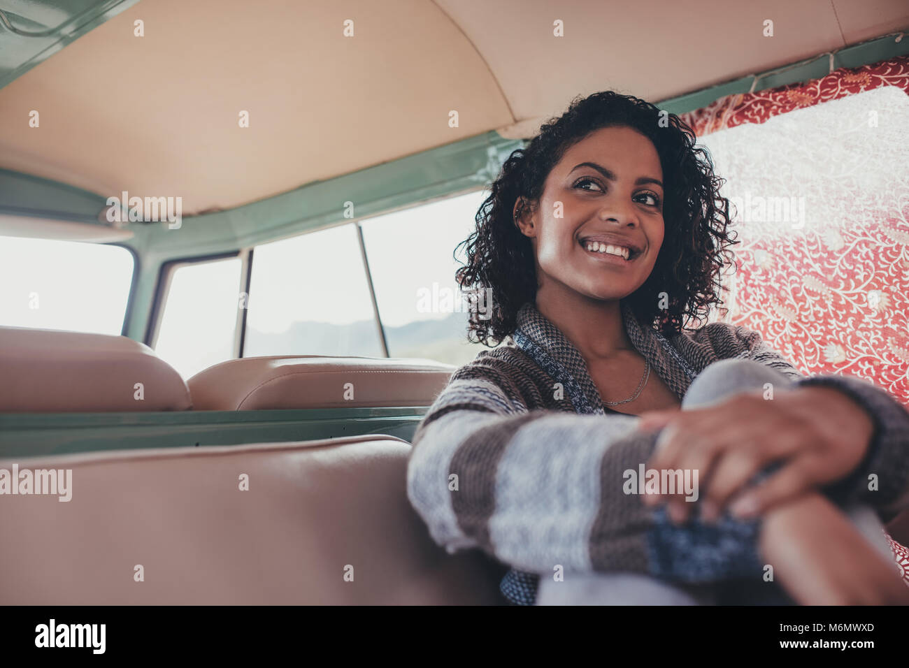 Lächelnde Frau auf Roadtrip Reisen mit einem Van. Afrikanische Frauen sitzen entspannt auf dem Rücksitz von Van und Wegsehen. Stockfoto