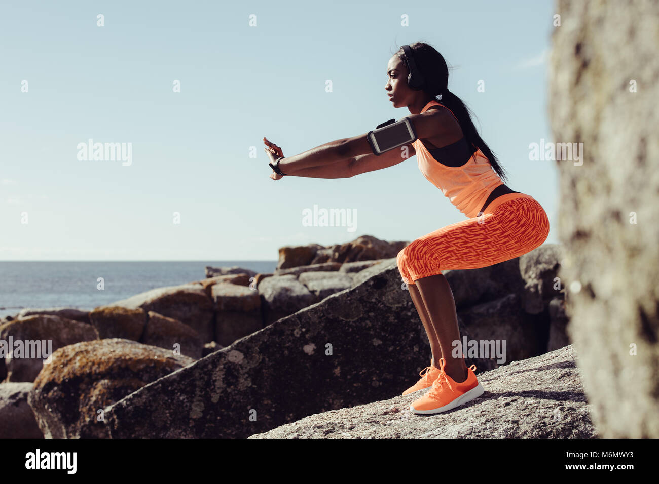Frau Läufer tun Dehnübungen. Frau tun Aufwärmen erstreckt sich auf den Felsen am Strand. Stockfoto