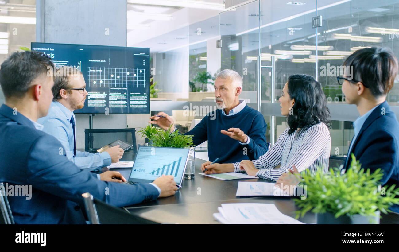 Senior Executive erklärt das Unternehmen Vision und Potenzial seiner Mitarbeiter. Sie sitzen am großen Tisch im Konferenzraum. TV-Bildschirm an der Wand Stockfoto