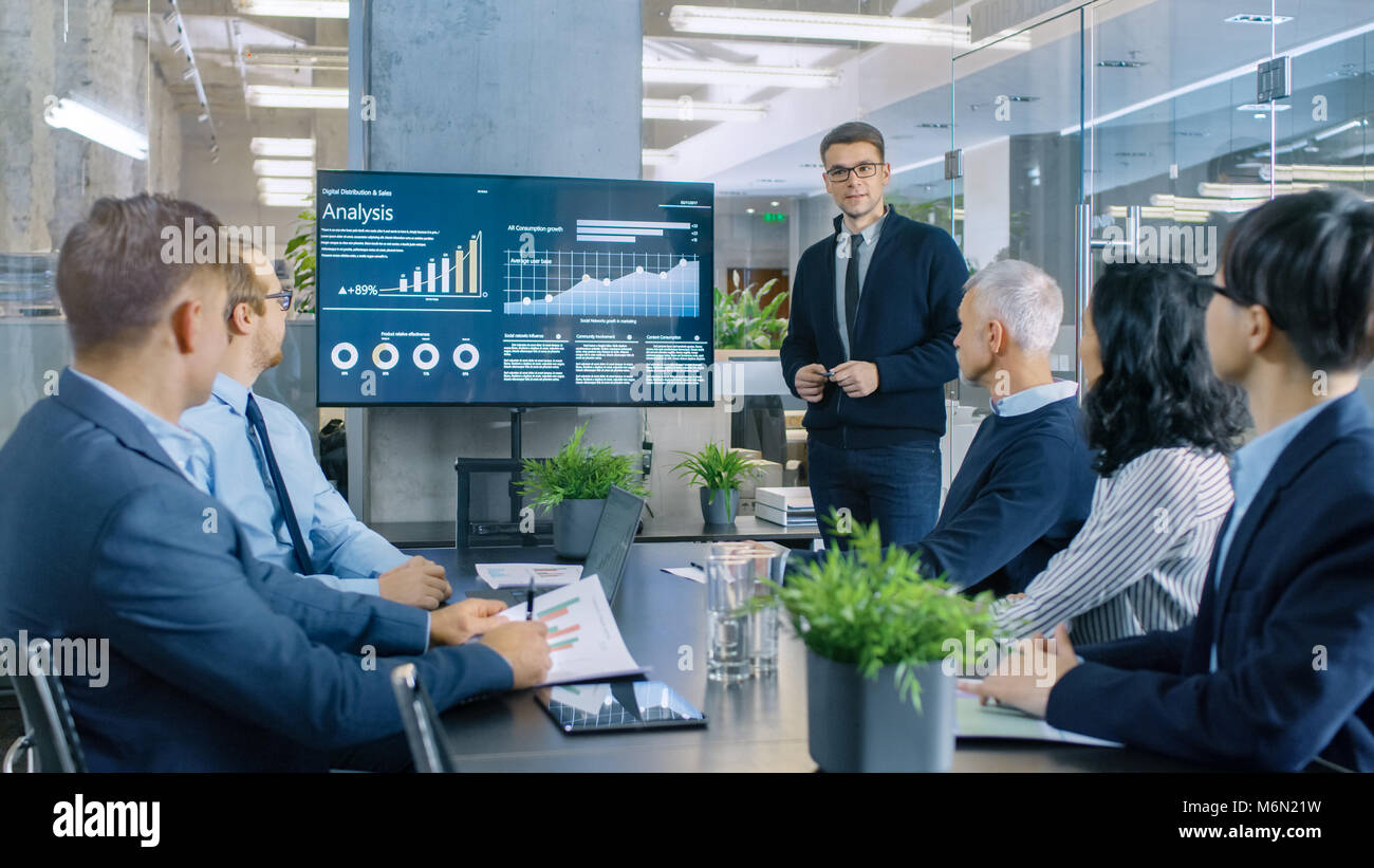 Junge Aktien Trader zeigt die Führungskräfte Cryptocurrency und Handel Markt Korrelation zeigen auf die Wand-TV. Stockfoto