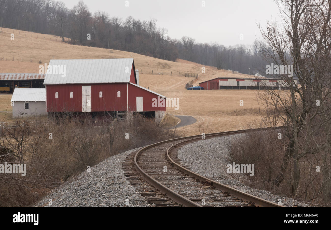 Rail Road tracks Kurve ihren Weg durch eine ländliche Landschaft der rote Ställe während einer trostlosen Winter. Stockfoto