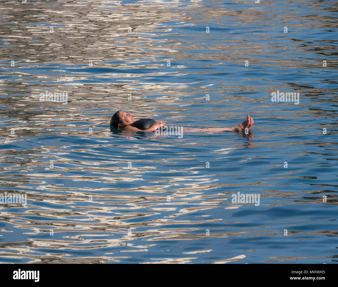 Weiße Frau, die auf ihrem Rücken im Tyrrhenischen Meer schwebt, Augen geschlossen, entspannt an einem heißen, sonnigen Tag. Stockfoto