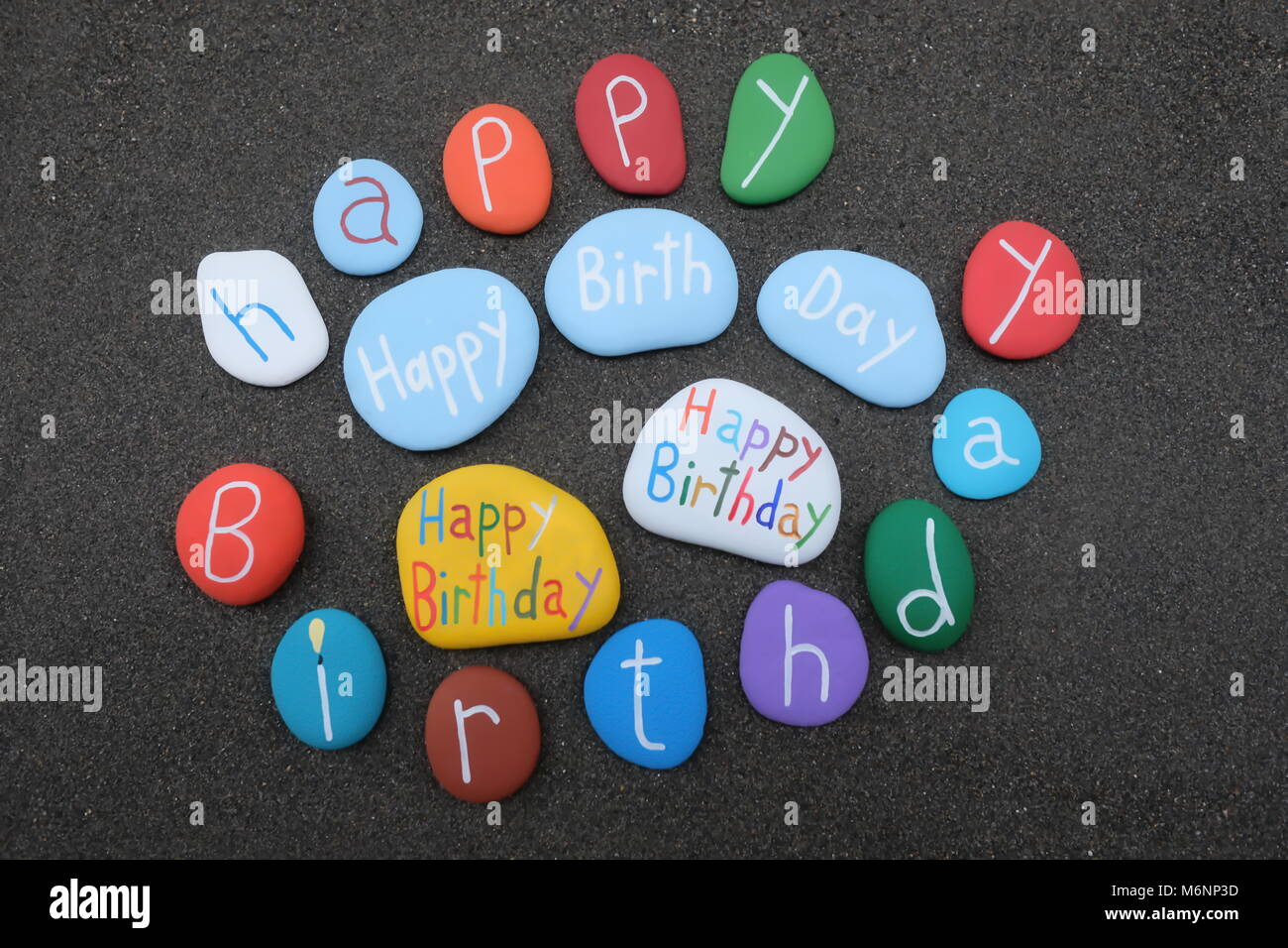 Viele Happy Birthday bunten Steinen gegenüber dem originalen schwarzen vulkanischen Sand Stockfoto